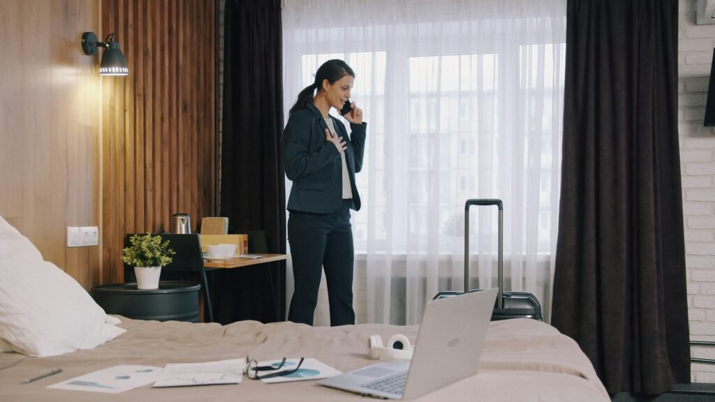 Business traveller on a phone call in a modern hotel room with a laptop and suitcase, a guest who could book her next stay through hotel direct bookings